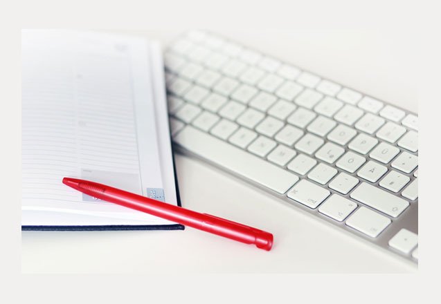 Heller Arbeitsplatz mit Tastatur, Notizblock und rotem Stift